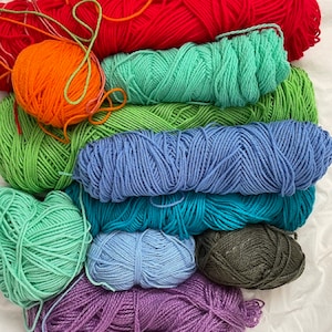 Pu&ograve; includere: Un mucchio di filato di vari colori, tra cui arancione, rosso, verde, blu, viola e grigio. Il filato &egrave; disposto a forma di arcobaleno.