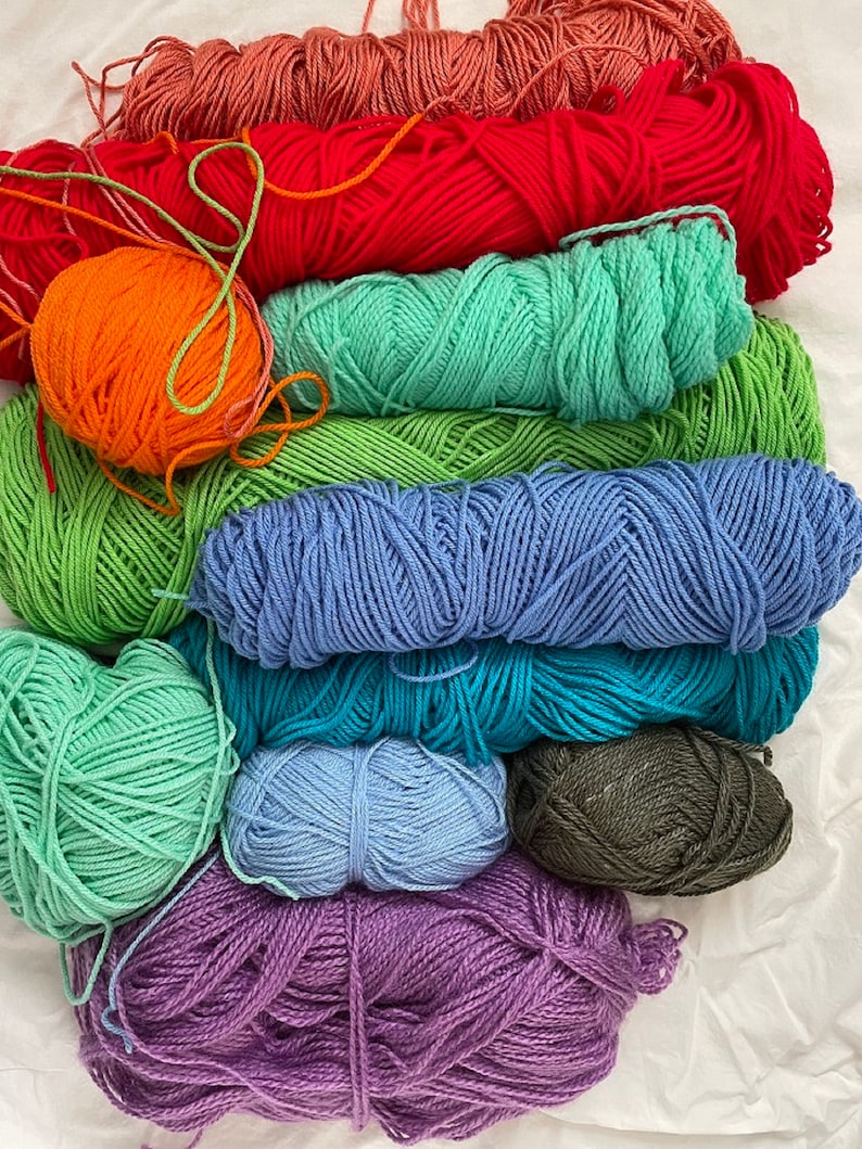 Pu&ograve; includere: Un mucchio di filato di vari colori, tra cui arancione, rosso, verde, blu, viola e grigio. Il filato &egrave; disposto a forma di arcobaleno.