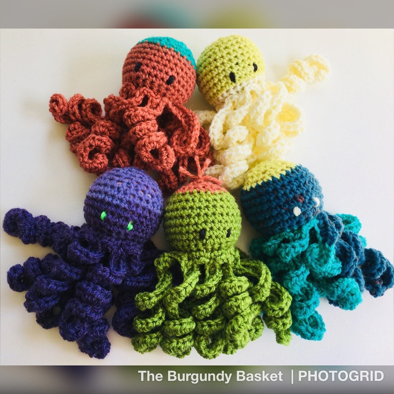 May include: Six crocheted octopus plushies in different colors, including purple, green, teal, cream, and brown. The octopus plushies have black eyes and are arranged in a circle on a white background.