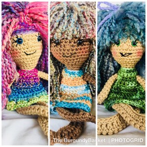 May include: Three crocheted dolls with colourful yarn hair and dresses. The dolls have different skin tones and eye colours. The dolls are sitting on a white surface.
