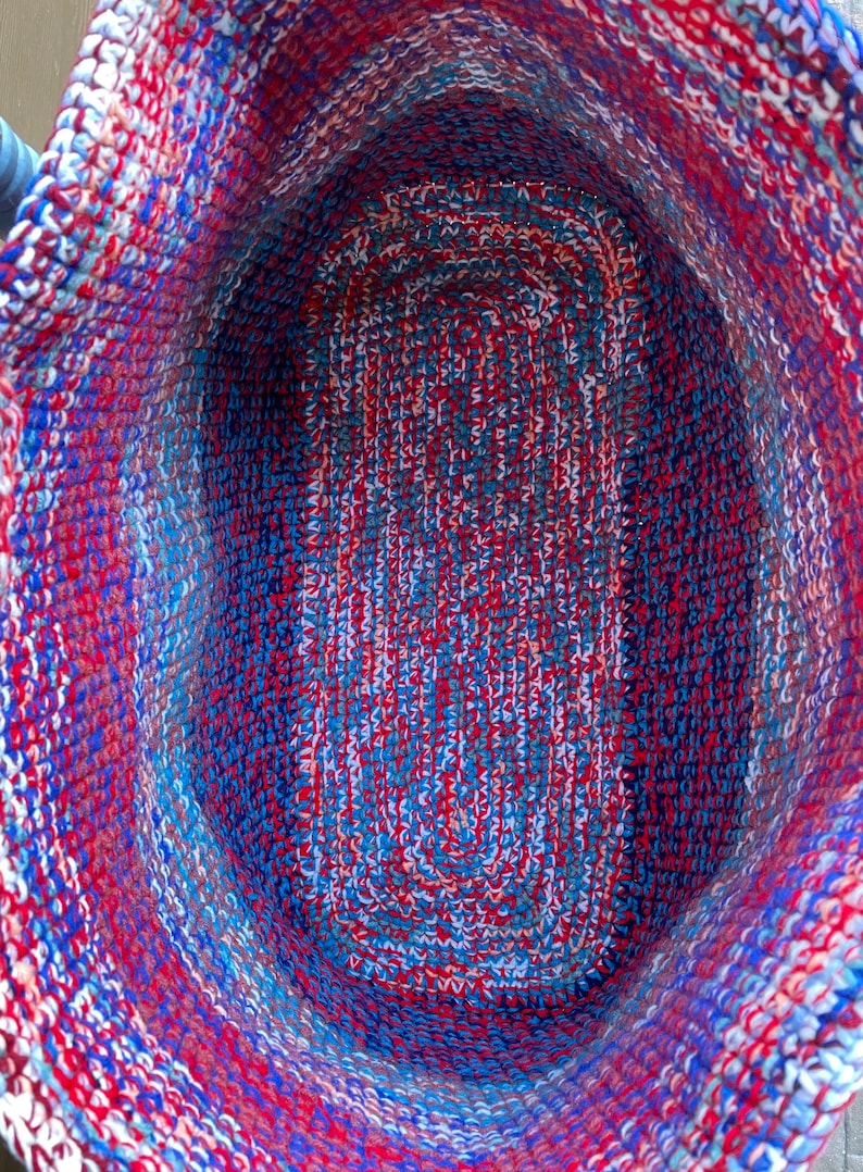 Pu&ograve; includere: Un cesto all'uncinetto con un motivo rosso, bianco e blu. Il cesto &egrave; vuoto e l'interno &egrave; visibile.