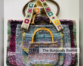 May include: A set of four crocheted bags in various shades of purple, blue, and green. The bags are nested inside each other, with the largest bag at the bottom and the smallest bag at the top. The bags have bamboo handles and are decorated with a colorful crocheted strap. The text "The Burgundy Basket" is visible on the image.