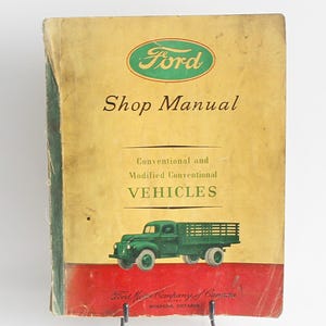 Könnte beinhalten: Ein Vintage Ford Werkstatt-Handbuch für konventionelle und modifizierte konventionelle Fahrzeuge. Der Umschlag zeigt ein grünes Ford-Logo und einen grünen LKW auf rotem Hintergrund.