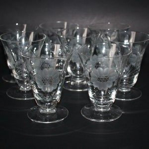 Peut inclure: Un ensemble de verres à pied en verre transparent. Chaque verre présente un motif floral gravé dans le verre. Les verres ont une base ronde et un bord évasé. Les verres sont disposés sur une surface sombre.
