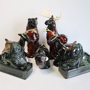May include: A selection of animal-shaped ornaments, featuring a bear, moose, deer, lion, and bison. The figurines are crafted from glass and ceramic, in shades of brown, black, and green. Some have gold-coloured antlers or horns.