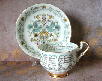 May include: A vintage teacup and saucer set. The white porcelain cup and saucer feature a teal and gold trim. The saucer has a bird and floral design. The cup says "Happy Anniversary" and lists anniversary gifts. A decorative gift.