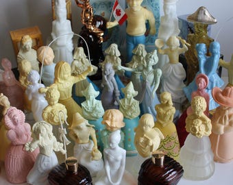May include: A collection of vintage perfume bottles, featuring various figurines in pastel colors. The figurines include a boy holding a Canadian flag, a woman skipping rope, and other figures. The bottles are brown and clear.
