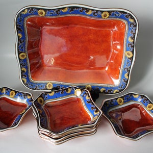 May include: A set of decorative serving dishes. The set includes a large rectangular dish and several smaller, uniquely shaped dishes. The dishes have a vibrant orange interior, a blue border with floral accents, and gold trim.
