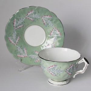 May include: A green teacup and saucer set with a delicate floral design. The cup and saucer are both trimmed with a gold band.