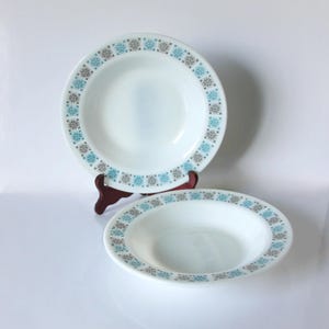 Puede incluir: Dos tazones de sopa de cerámica blanca con un patrón geométrico azul y gris alrededor del borde.