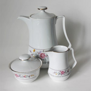 Puede incluir: Un juego de té de porcelana blanca con diseños florales. El juego incluye una tetera, una jarra de crema y un azucarero.