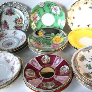 Könnte beinhalten: Eine Sammlung von Vintage-Teetassen und Untertassen mit verschiedenen floralen und dekorativen Mustern. Die Untertassen sind in den Farben Grün, Rosa, Gelb und Weiß gehalten.