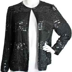 May include: A black sequined jacket with a long sleeve and open front. The jacket is made of a soft, flowing fabric and is adorned with intricate beading and sequins.