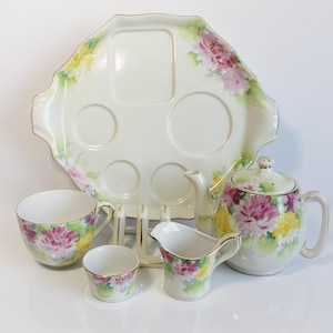Könnte beinhalten: Ein Teeservice aus Porzellan mit einem großen Serviertablett mit geformten Vertiefungen, einer Teekanne, einem Milchkännchen, einer Teetasse und einer kleinen Schale. Jedes Teil ist mit handgemalten rosa und gelben Chrysanthemen verziert.