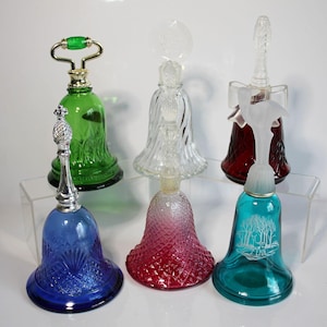 Puede incluir: Una colección de seis frascos de perfume decorativos de vidrio en forma de campana. Las botellas son de varios colores, incluyendo verde, azul, rojo y transparente. Algunas tienen tapones ornamentados, y una tiene una escena de bosque grabada en el vidrio.