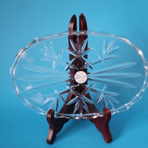 Puede incluir: Un plato ovalado de servir de vidrio transparente con un diseño de vidrio cortado. El plato está sobre un soporte de madera.