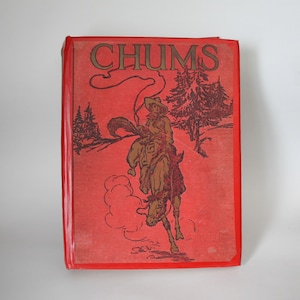 May include: A red hardback book titled CHUMS with a dark brown illustration on the front cover depicting a person riding a bucking horse in a landscape with pine trees. The book has a glossy red spine and a textured red cover material.
