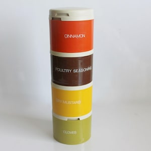 Puede incluir: Un especiero apilable con cuatro secciones de colores: naranja, marrón, amarillo y verde. Cada sección está etiquetada con texto blanco: "Cinnamon", "Poultry Seasoning", "Dry Mustard" y "Cloves". Tiene una tapa blanca.