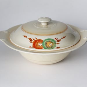 Puede incluir: Un plato de servir de cerámica blanca con tapa. El plato tiene un diseño floral con flores naranjas y verdes.