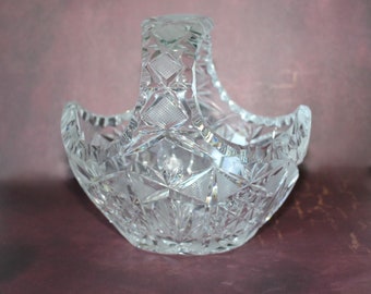 May include: A clear glass bowl with a cut glass design and a handle. The bowl is empty and has a shiny finish.