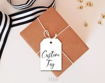 May include: A white gift tag with black calligraphy that reads "Custom Tag". The tag is tied with twine to a brown paper gift box. The box is sitting on a white surface with black and white striped ribbon.