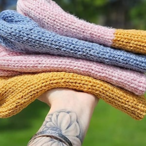 May include: A stack of four knitted hats in different colors. The bottom hat is mustard yellow, the next is pink, then blue, and the top hat is pink with a mustard yellow brim.