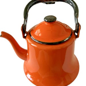 May include: A bright orange enamel tea kettle with a glossy finish, featuring a black curved handle, a matching orange lid with a black knob, and a curved spout. The rim of the lid and the base of the handle show minor black metal detailing.