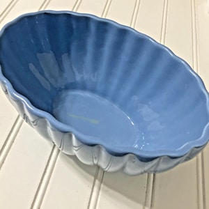 May include: A blue ceramic oval serving dish with a scalloped edge. The dish has vertical ridges on the sides and a glossy finish. The interior is a lighter shade of blue.