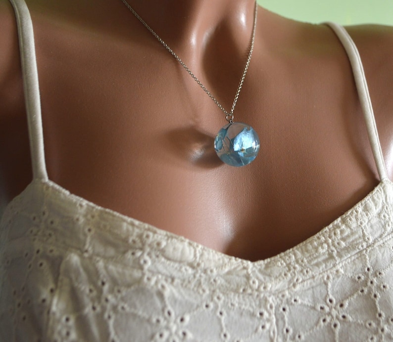 May include: A silver chain necklace with a round pendant containing blue pressed flowers encased in clear resin.