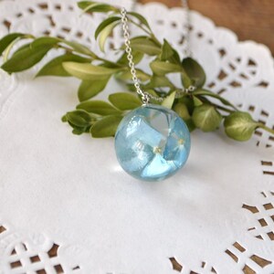 May include: A silver chain necklace with a round pendant featuring blue pressed flowers encased in clear resin.