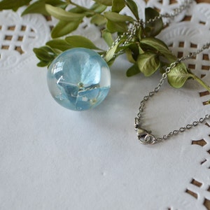 May include: A delicate silver chain necklace with a clear glass orb pendant containing a pressed blue flower.