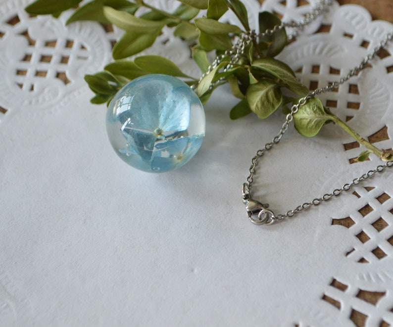 May include: A delicate silver chain necklace with a clear glass orb pendant containing a pressed blue flower.
