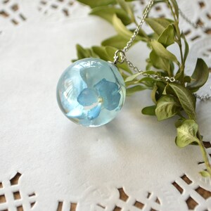 May include: A silver chain necklace with a clear glass sphere pendant containing a preserved blue flower.