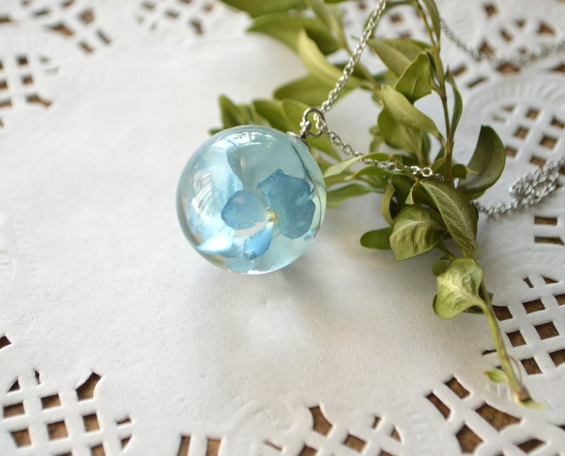 May include: A silver chain necklace with a clear glass sphere pendant containing a preserved blue flower.