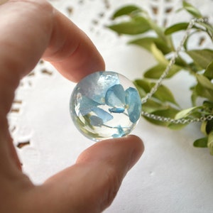 May include: A silver chain necklace with a clear glass pendant containing blue pressed flowers.