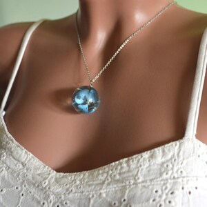 May include: A silver chain necklace with a round pendant featuring a blue flower encased in clear resin.
