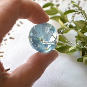 May include: A silver chain necklace with a clear glass pendant containing a pressed blue flower.