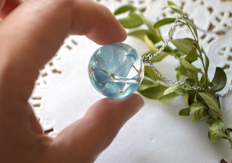 May include: A silver chain necklace with a clear glass pendant containing a pressed blue flower.