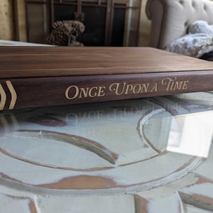 This image of a close up detail on the spine of a book shape cutting board shows it's walnut design with maple inlaid title of Once Upon a Time.