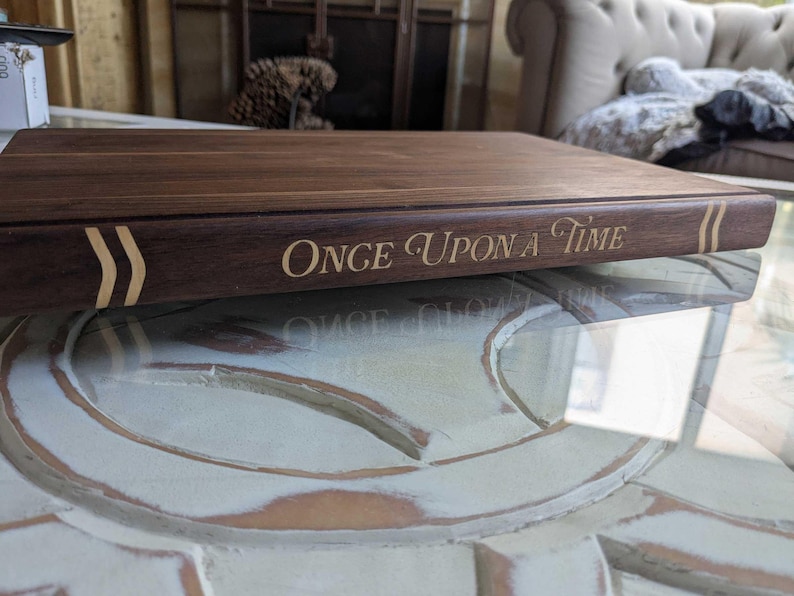 This image of a close up detail on the spine of a book shape cutting board shows it's walnut design with maple inlaid title of Once Upon a Time.