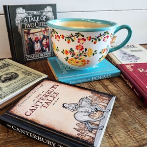 A flowery teacup sits on top of the book Coaster Emily Dickenson Poems, surrounded by other classic titled books