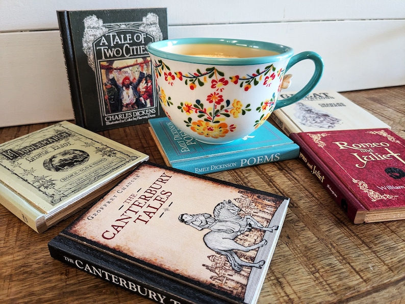 A flowery teacup sits on top of the book Coaster Emily Dickenson Poems, surrounded by other classic titled books