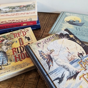 A set of childrens book themed book coasters sit arranged on a stressed wood table.  Grimms fairy tales, red's riding hood, wind in the willows, Rapunzel, and the House at Poo Corner in view.