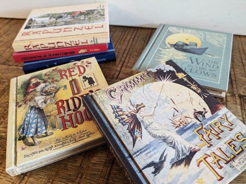 A set of childrens book themed book coasters sit arranged on a stressed wood table.  Grimms fairy tales, red's riding hood, wind in the willows, Rapunzel, and the House at Poo Corner in view.