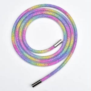 Puede incluir: Una correa de teléfono enrollada, multicolor, con cierres de metal plateado. La correa presenta un degradado de colores, incluyendo rosa, amarillo, verde y morado. La correa está diseñada para ser usada alrededor del cuello o la muñeca.