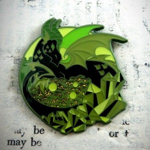 May include: Green enamel pin featuring a black dragon with green wings and a green crystal design. The dragon is curled around the crystals, which are outlined in black.