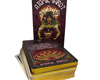 May include: A deck of Atomic Tarot cards with a matching box. The box features a woman with green skin and a crown. The cards have gold edges and the words "Atomic Tarot" are printed on the box and the cards.