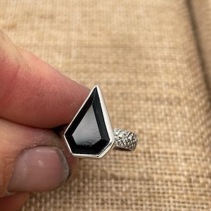 May include: A silver ring with a black gemstone in a geometric shape.