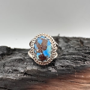 May include: A silver ring with a blue and brown oval turquoise stone set in a rope design band.