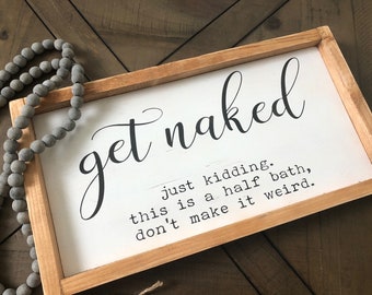 May include: A rectangular wooden sign with the words "get naked" in a cursive font. Below, smaller text reads "just kidding. this is a half bath, don't make it weird." A strand of gray beads is draped on the left.